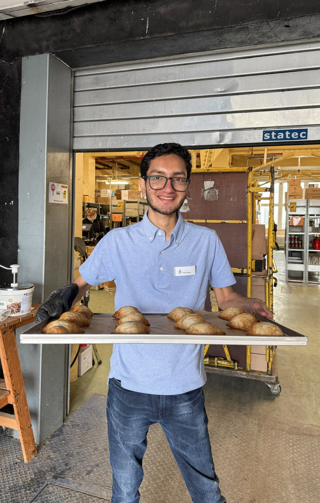 Mitarbeiter steht im Kaffeelager und hält ein Blech mit frisch gebackenen Sfogliatelle